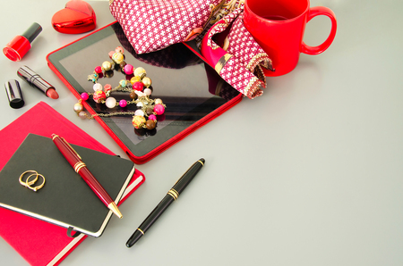 Woman modern desktop with red accessories: tablet, dairy with pen, , cosmetic, jewellery, luxury neck scarf,   cup of coffee in red mug. Flay lay. Copyspace.の写真素材