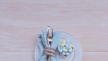 Happy Easter concept. Top view of beautiful spring table settings in pastel tone, blue linen napkin with rustic napkin ring  and bowl with chocolate Easter eggs on wooden background. Copy space.の写真素材