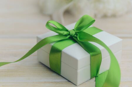 White gift box with green ribbon and bow on light wooden background.
