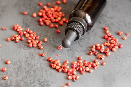 Pink pepper essential oil and pink peppercorns on black concrete background.のeditorial素材