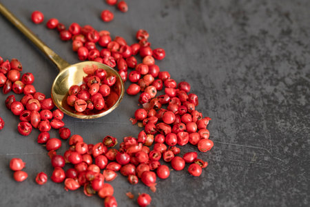 Pink pepper in a gold spoon on black large background. Copy space