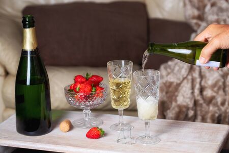 Champagne pouring into the glass and strawberry on the table in living room for romantic date concept background. Saint Valentines day celebrationの写真素材