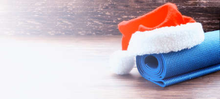 Close up of blue mat with Santa Clause hat on wooden background. Best Christmas gift for active person. Yoga xmas concept. Copy space.の写真素材