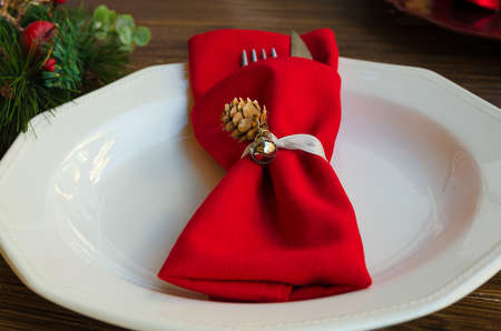Close up of napkin ring with cone and bell on white plate. Elegant Christmas decoration for festive...
