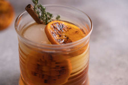 Close up of Whiskey sour cocktail with tangerine slices and ice cubes decorated with cinnamon and thyme.の写真素材