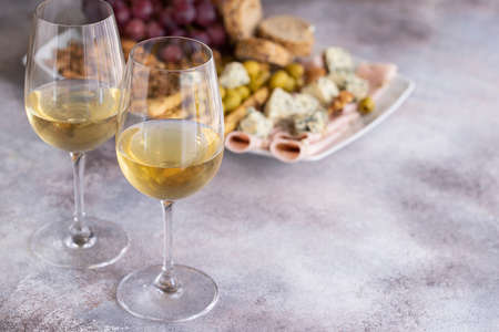 Two glasses of white wine and plate with different snacks. Blue cheese, olives, baguette slices, grissini, ham, grapes and nuts. Wine snacks set background.Copy spaceの写真素材