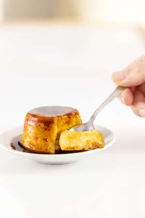Creme caramel dessert or flan on white table. Hand holding a piece of delicious flan.