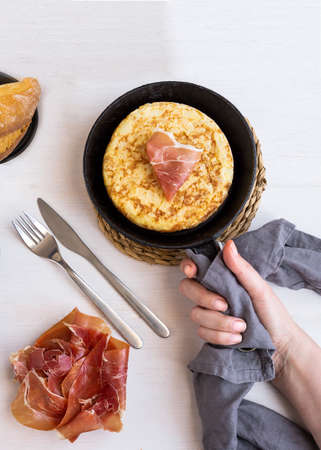 Women hand holding frying pan with Tortilla, Spanish omelette made with eggs and potatoes and servew with jamon, iberian ham. Top view.の写真素材