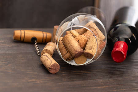 Red wine bottle, wine glass with wine corks and corkscrew on wooden table. Drinking wine concept.の写真素材