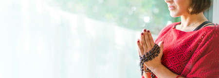 Beautiful brunette yogi girl holding hands with mala beads in namaste. Meditation and yoga practice...