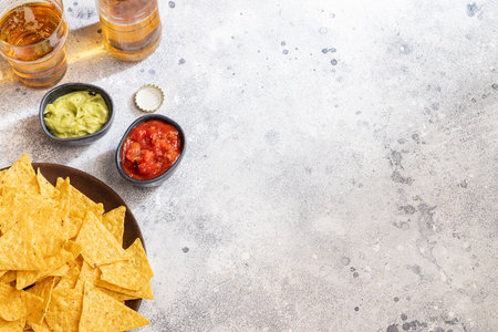 Famous Mexican snack, nachos with guacamole, red chilli sauce and beer on cement background. Top view.の写真素材
