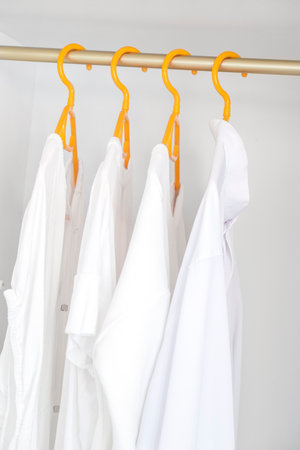 White shirts hanging on rack in wardrobe closet. Female different clothes in on yellow hangs