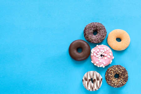Different donuts with chocolate frosted, pink glazed and sprinkles on blue background with copy space. Assortment of various colorful donuts. top viewの写真素材
