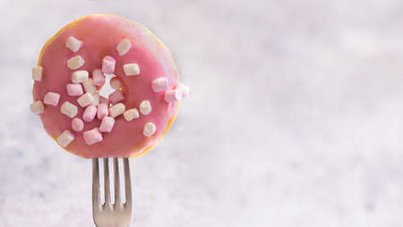 Close up of fork with pink glazed donut with marshmallow .Large donut background with copy space for bannerの写真素材