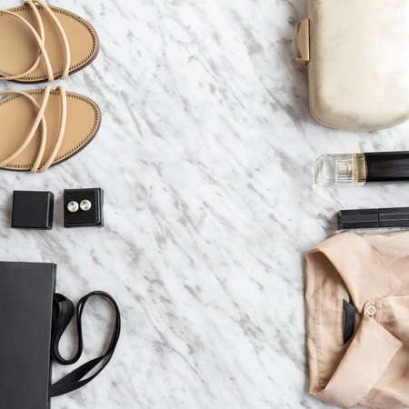 Fashion and beauty blog concept. Woman clothes and accessories: beige blouse, luxury sandals and clutch, perfume and cosmetic marble office desk background. trendy flat layの写真素材