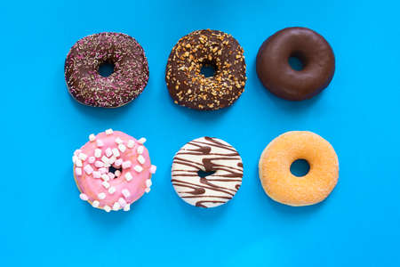Different donuts with chocolate frosted, pink glazed and sprinkles on blue lbackground with copy space. Assortment of various colorful donuts. top viewの写真素材