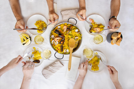 Friends all together enjoy having a dinner. Friendship meeting lifestyle background. Top view of table setting with Spanish dish paella.の写真素材