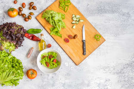 Cutting board with different vegetables, olive oil and spices, knife and bowl for salad. Healthy...