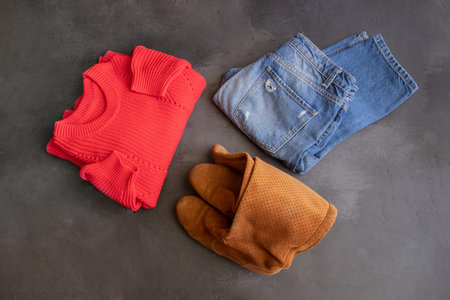 Fashion winter outfit. Blue jeans, red knitted sweater and brown shoes on concrete background.