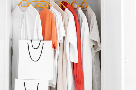 Collection of clothes hanging on rack in wardrobe in dressing room and white paper shopping bags. Fashion shopping concept background.の写真素材