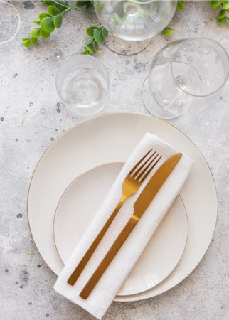 Elegant table setting, white plate with gold cutlery and wine glasses on cement background. scandinavian styleの写真素材