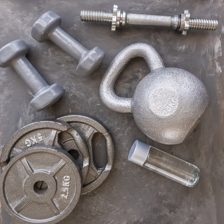 Weight plates for barbell, gray dumbbells, kettlebell and water bottle in cement floor in gym.の写真素材