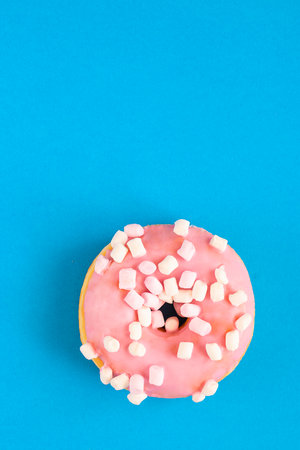 Close up of pink glazed donut with marshmallow on blue modern background. copy-spaceの写真素材