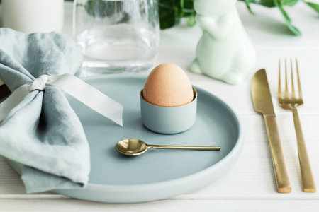 Happy Easter table setting with traditional Easter decoration : white bunny, natural egg in mint green plate with gold cutlery. Scandinavian style backgroundの写真素材