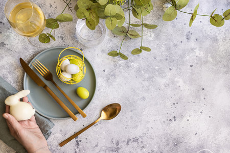Happy Easter table setting: mint green plate with gold cutlery and woman hand with bunny, painted...