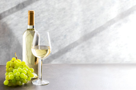 White wine bottle, wine glass and grape on gray concrete background. Wine making and wine tasting concept.の写真素材