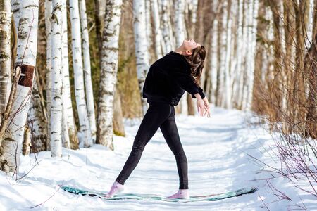 Yoga in the snow. Girl practicing yoga in the Park. Time of year winter. Snow-covered trees.の写真素材