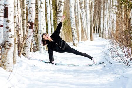 Yoga in the snow. Girl practicing yoga in the Park. Time of year winter. Snow-covered trees.の写真素材
