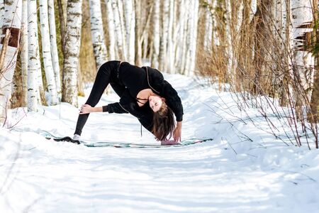 Yoga in the snow. Girl practicing yoga in the Park. Time of year winter. Snow-covered trees.の写真素材