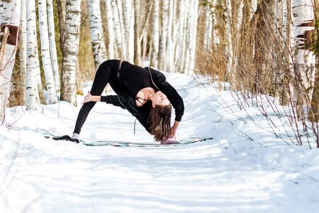 Yoga in the snow. Girl practicing yoga in the Park. Time of year winter. Snow-covered trees.の写真素材