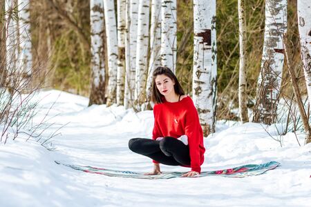 Yoga in the snow. Girl practicing yoga in the Park. Time of year winter. Snow-covered trees.の写真素材