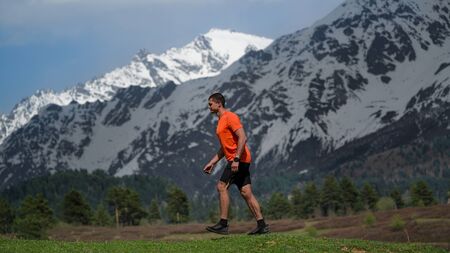 The guy goes uphill on a green meadow sticking out veins on the hands and feet in the background the snowの写真素材