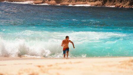 The guy is running away from the waves of the ocean in shorts on the beach sun heatの写真素材