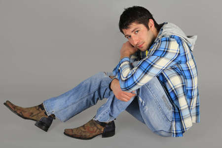 Man in jeans and a plaid shirt sitting on the floor    の写真素材
