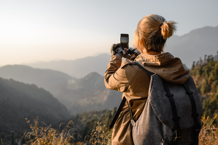Backpacker young girl make photo by phone in the mountainsの写真素材