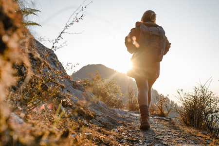 Young girl with backpack walking on the mountains path in the sunlightの写真素材