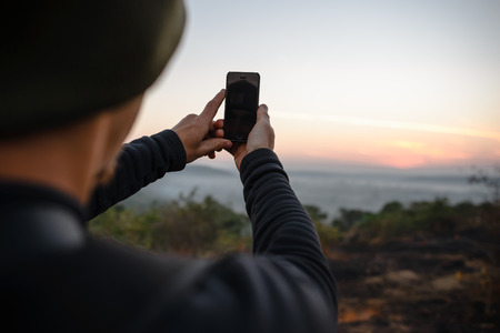 Travel photographer taking a shots by mobile phone at sunrise. Hipster with a little camera in the good light. Smartphone in handsの写真素材