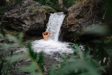 Young girl with no dress washing in natural waterfallの写真素材