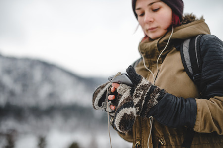Young woman listening the music by the headphones. Mobile phone in her hands. Winter mountains on the background.の写真素材