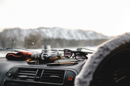 Notebook, glasses and film camera on the dashboard in the car. Closeup shot, mountains on the backgroundの写真素材