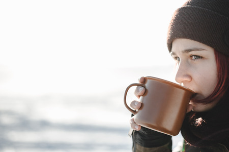 Young woman drinking hot beverage outdoors. Good light in the beginning of spring.の写真素材