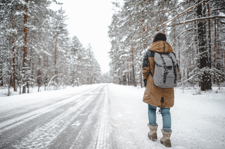 Girl with backpack walk alone near the road in snow forest.の写真素材