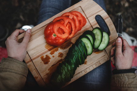 Sliced fresh tomatoes and cucumbers on the board. Hands hold the knifeの写真素材