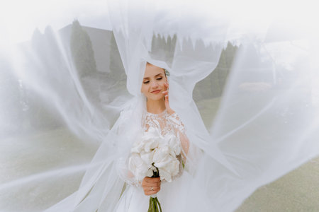 Happy beautiful bride under veil closeup. Beautiful bride shows makeup and hairstyle. Bride in a white dress plays with her veil.の写真素材