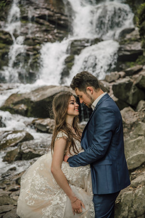 Portrait of a happy bride and groom near a waterfall. Bride and groom. Wedding photo session in nature. Photo session in the forest of the bride and groom.の写真素材