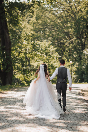 Groom and bride in the garden. Spring wedding in the park. Happy wedding couple running in the park. Stylish and beautiful. Photo from the back. Princess dress.の写真素材